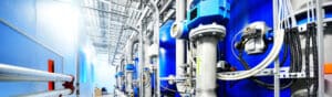 A modern industrial facility with large blue tanks, pipes, and machinery. The setup is clean and organized, displaying a complex network of metal tubes and gauges, indicating a high-tech processing environment.