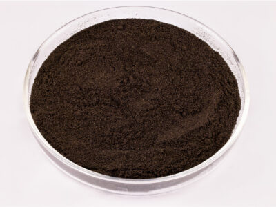 A clear glass petri dish filled with fine, dark brown or black powder sits on a white background.