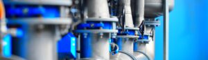 Close-up view of industrial metal pipes and blue valve components in a modern facility, with a blurred blue background.