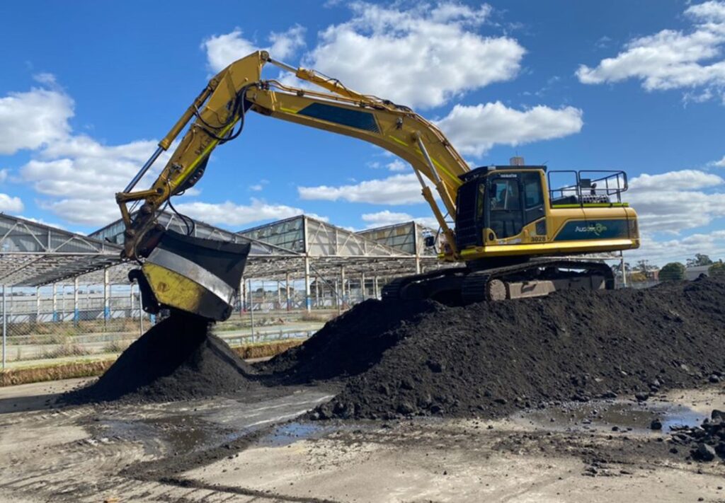 An excavator fitted with a screening bucket blending treated soil.