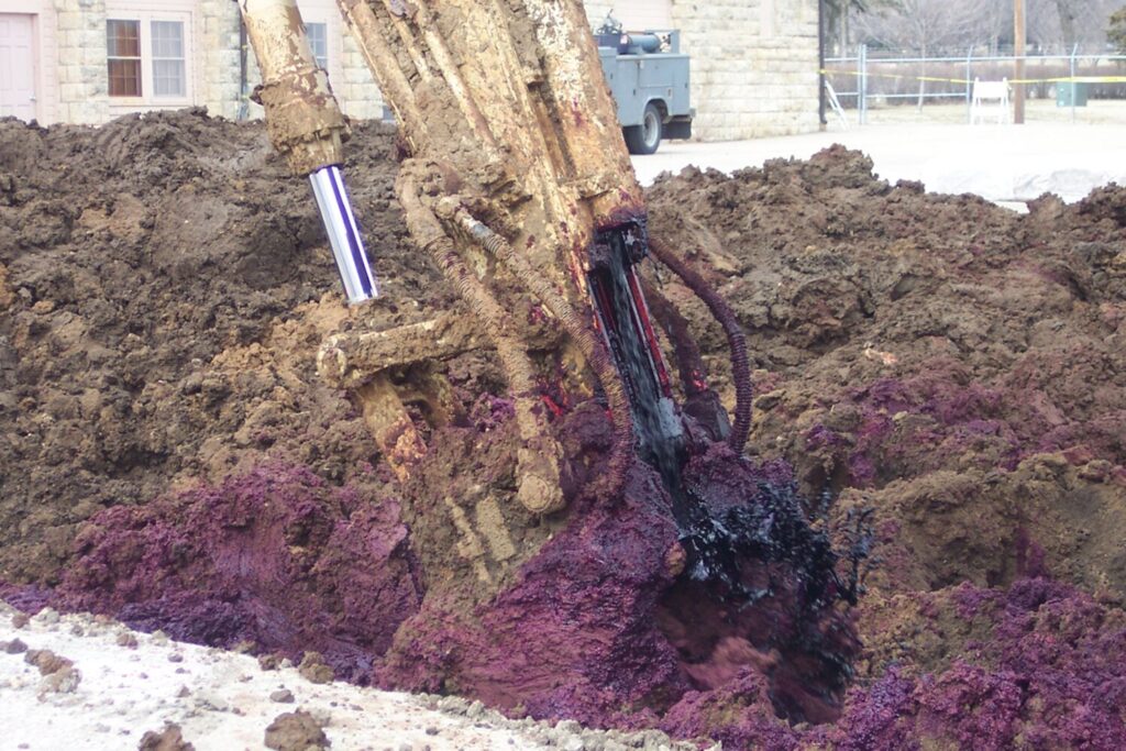 An excavator mixing purple permanganate reagent into contaminated soil during in situ soil mixing.