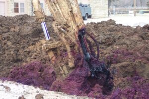 An excavator mixing purple permanganate reagent into contaminated soil during in situ soil mixing.