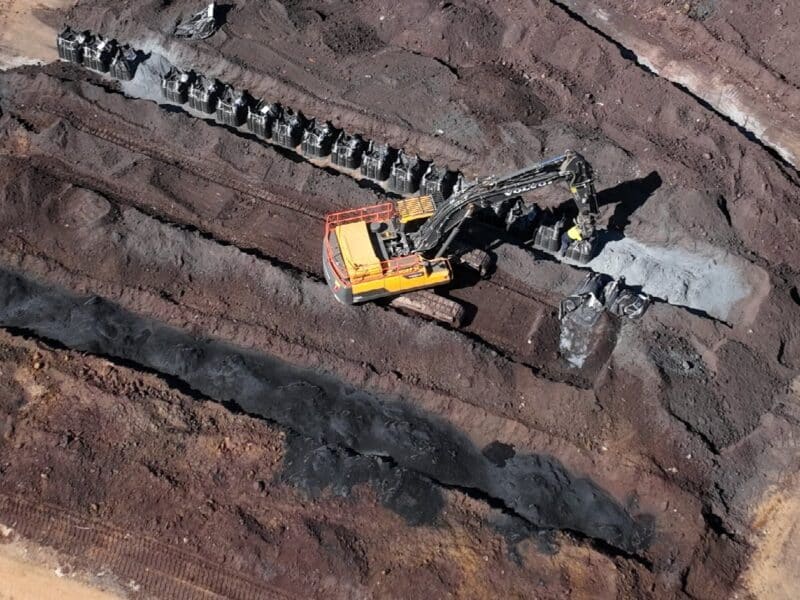 Aerial view of an excavator blending sorbent from rows of bulk bags into windrows of contaminated soil.