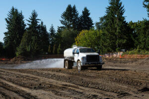 A water truck spraying diluted RemActiv over a soil treatment area during field application.