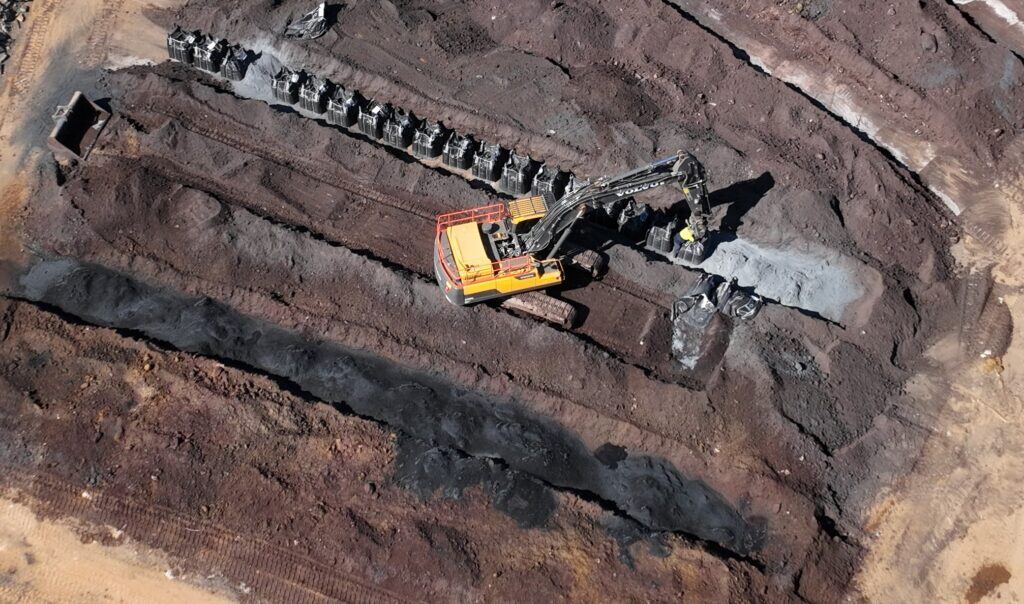 Aerial view of an excavator blending sorbent from bulk bags into a windrow of contaminated soil.