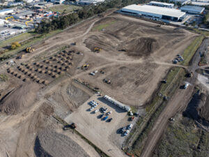 Aerial view of a remediation site with graded work areas and stockpiles beside an industrial estate.