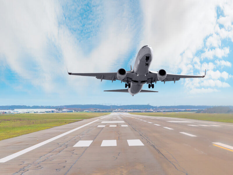 A commercial airplane taking off over an airport runway.