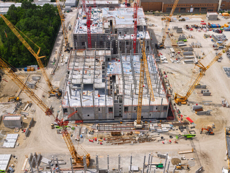 Aerial view of a large building under construction with tower cranes and staged precast materials.