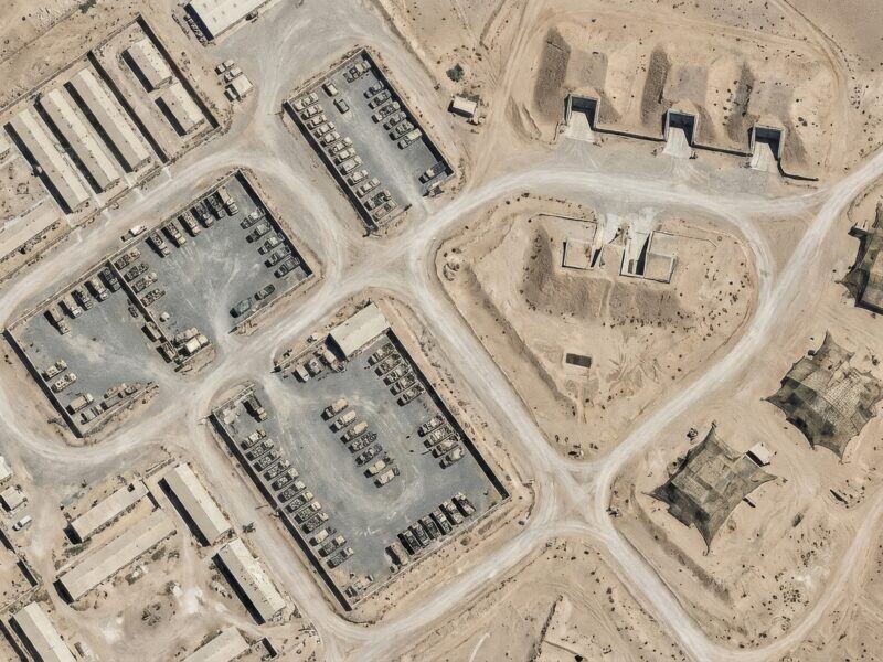 Aerial view of a military installation with vehicle depots and hardened shelters.