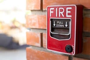 Red fire alarm pull station mounted on a brick wall, with the word “FIRE” and instructions to “PULL DOWN” visible.
