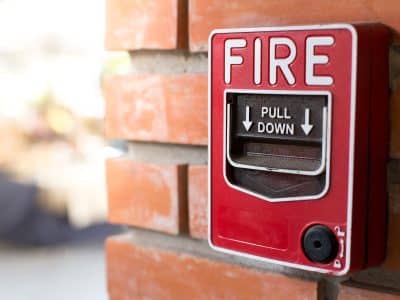 Red fire alarm pull station mounted on a brick wall, with the word “FIRE” and instructions to “PULL DOWN” visible.
