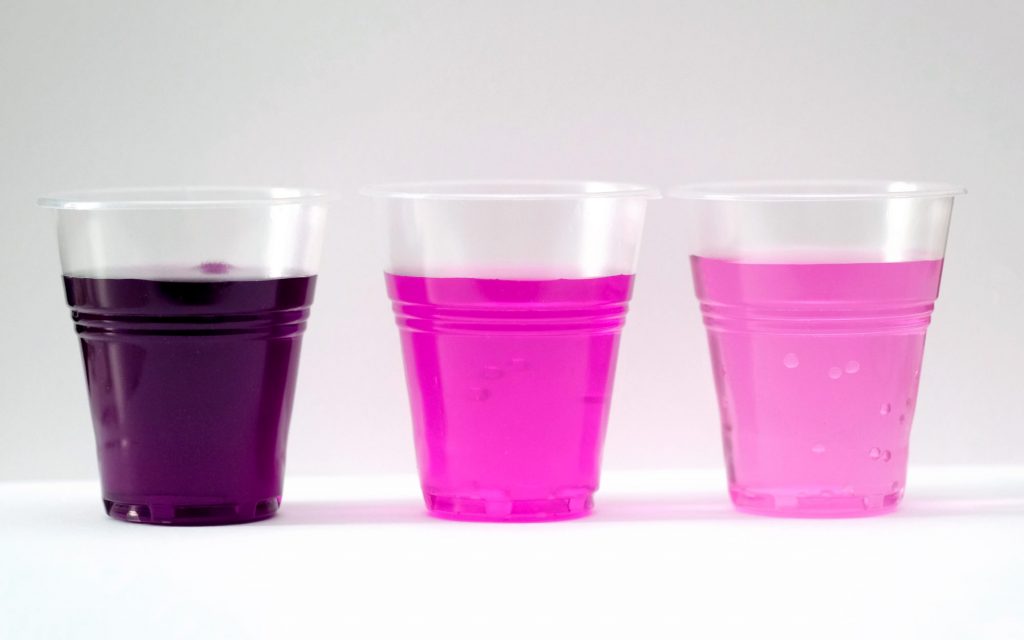 three clear plastic cups with different shades of liquid from purple to pink